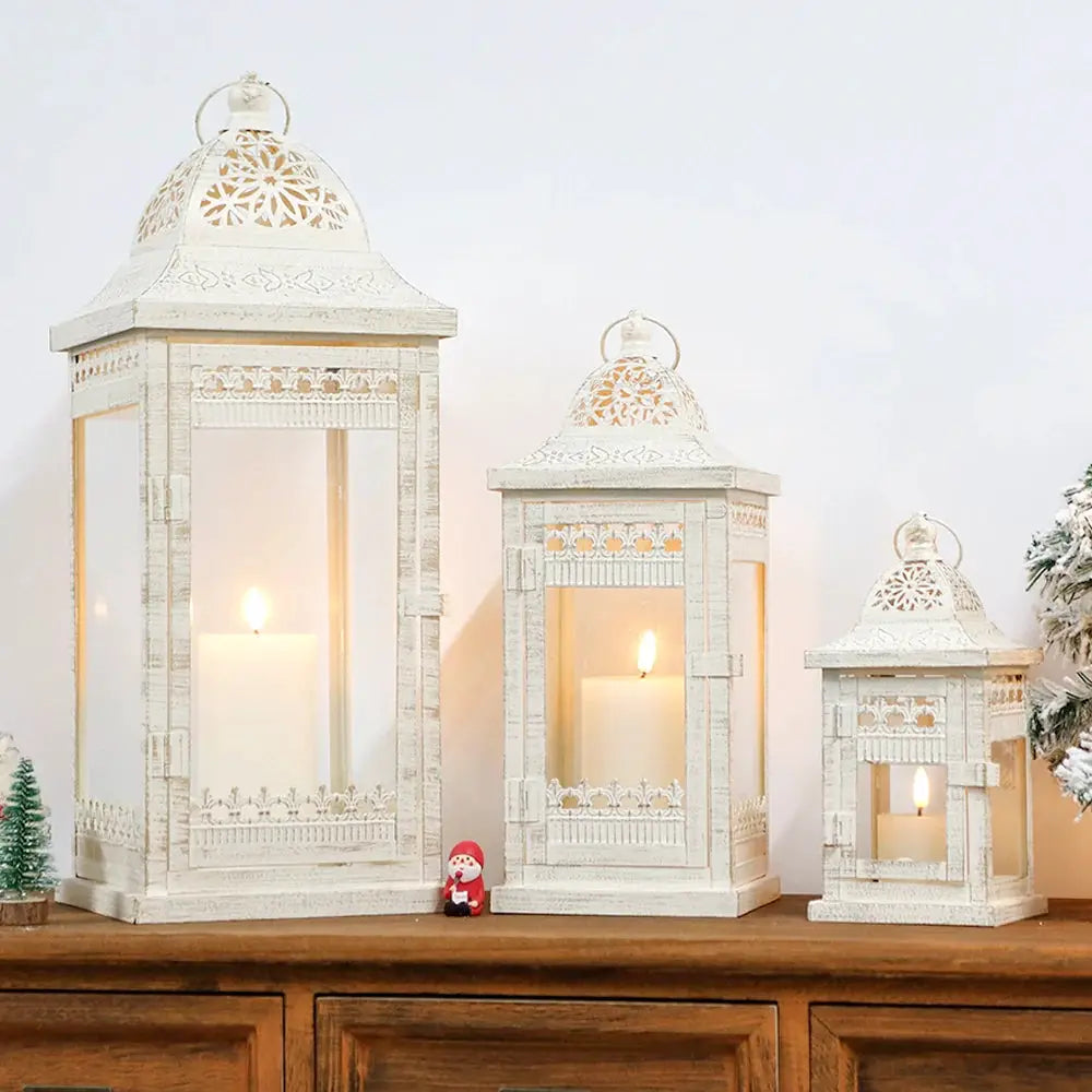 Set of 3 beige vintage metal candle lanterns with glass panels and decorative lattice, candles lit.