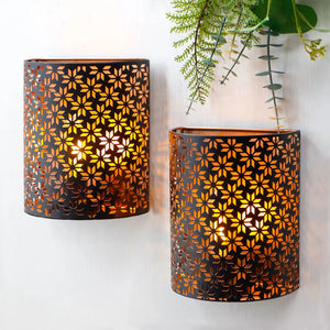 Set of 2 snowflake-pattern wall sconces; dark metal with warm amber glow