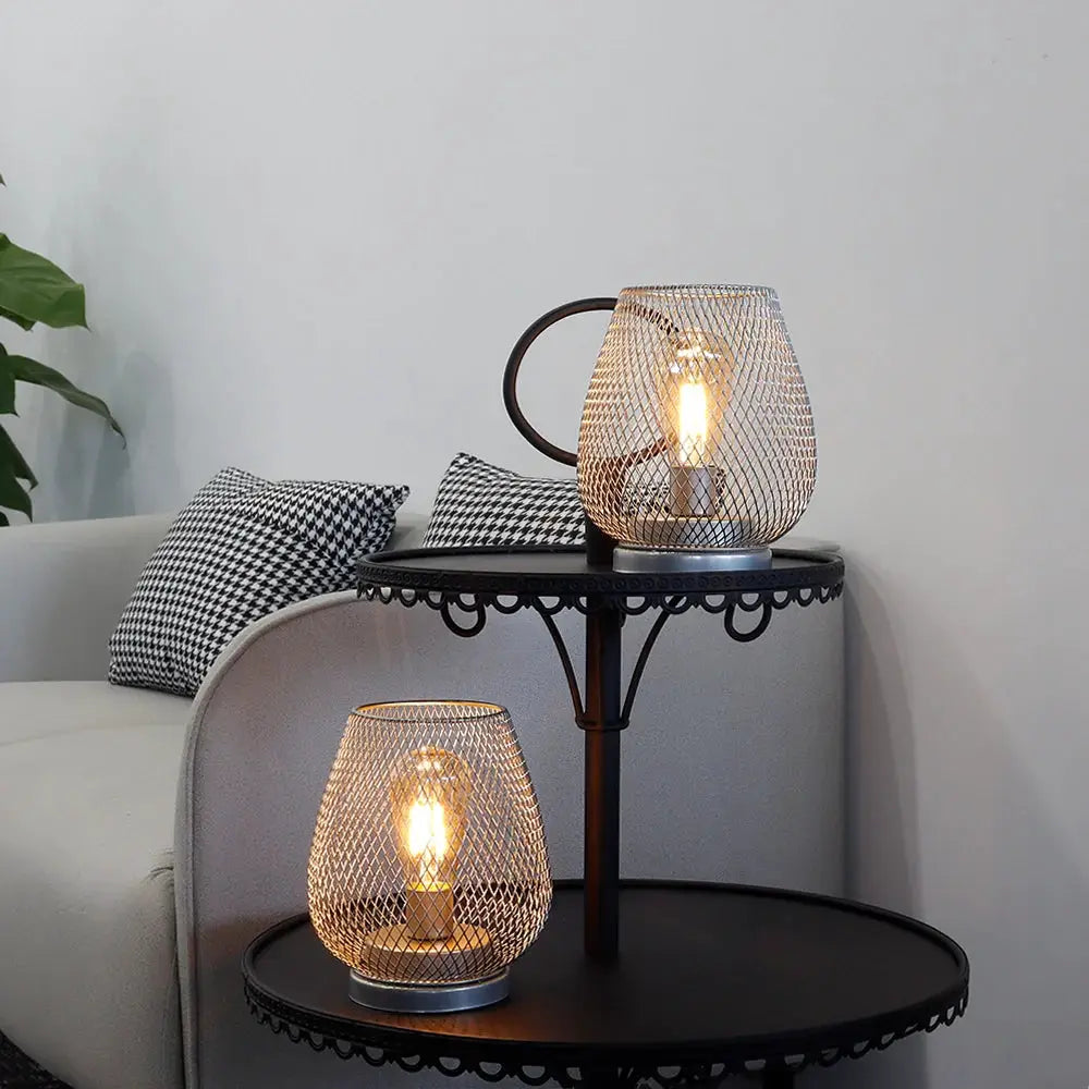 Set of 2 silver metal cage LED lanterns, battery-operated, on a round black side table.