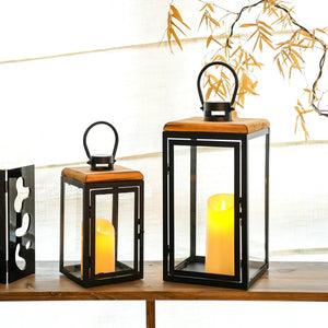 Set of 2 JHY DESIGN decorative candle lanterns, 16in & 11in tall, black metal with wood tops and glass panels.
