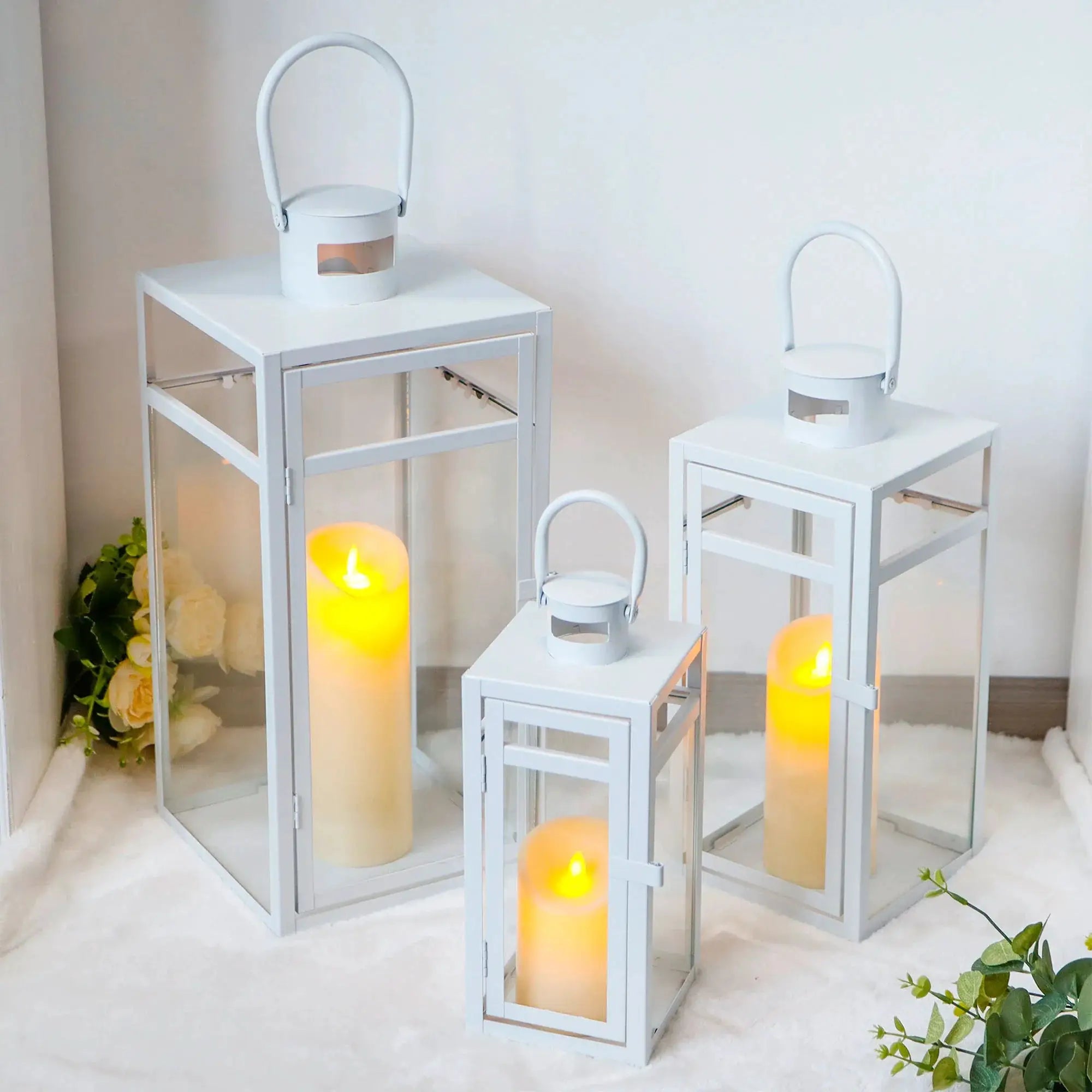 Set of 3 white metal candle lanterns in varying heights displayed on white tables.