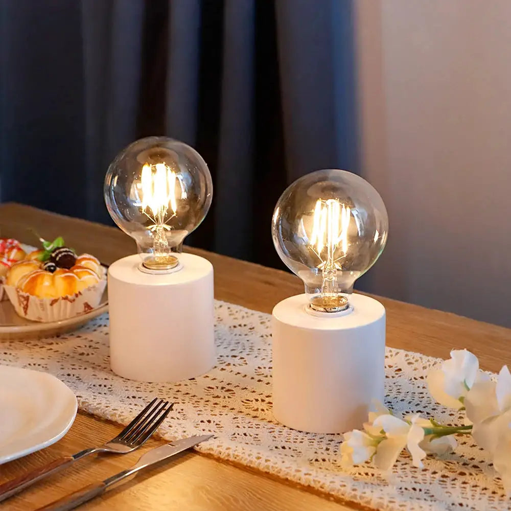 Set of 2 7-inch-tall white battery-powered table lamps with clear glass bulbs and cylindrical bases.