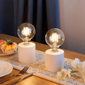 Set of 2 7-inch-tall white battery-powered table lamps with clear glass bulbs and cylindrical bases.