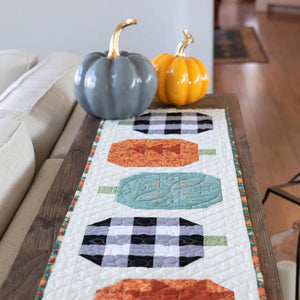 Holiday Quilted Table Runner Kit Bundle quilt kit on a wooden table with two pumpkins, blue-gray and orange
