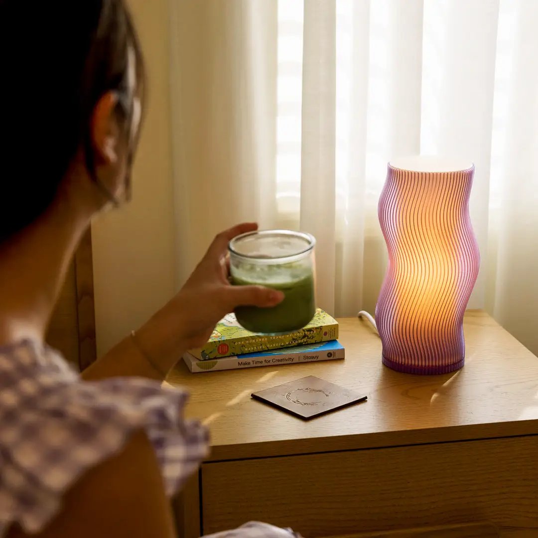 Woogie Table Lamp by Terra Labs, purple-pink gradient glass lamp with a wavy silhouette on a wooden nightstand.