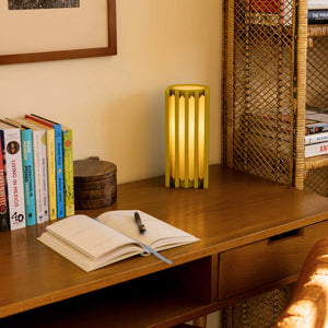 Radiator Table Lamp by Terra Labs; lime-green metal lamp with vertical slats casting warm light on a desk.