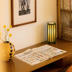 Radiator Table Lamp, green metal frame, emits warm glow on a wooden desk beside a colorful magazine.