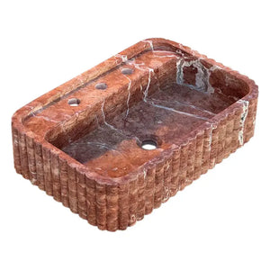 Red travertine wall-mount bathroom sink with ribbed textured exterior and rectangular basin.