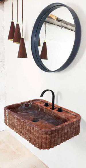 Red travertine wall-mount bathroom sink by Villohome, ribbed texture with a round dark-framed mirror