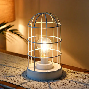 9.5"H white decorative metal cage table lamp with an exposed bulb, battery-operated, vintage-style.