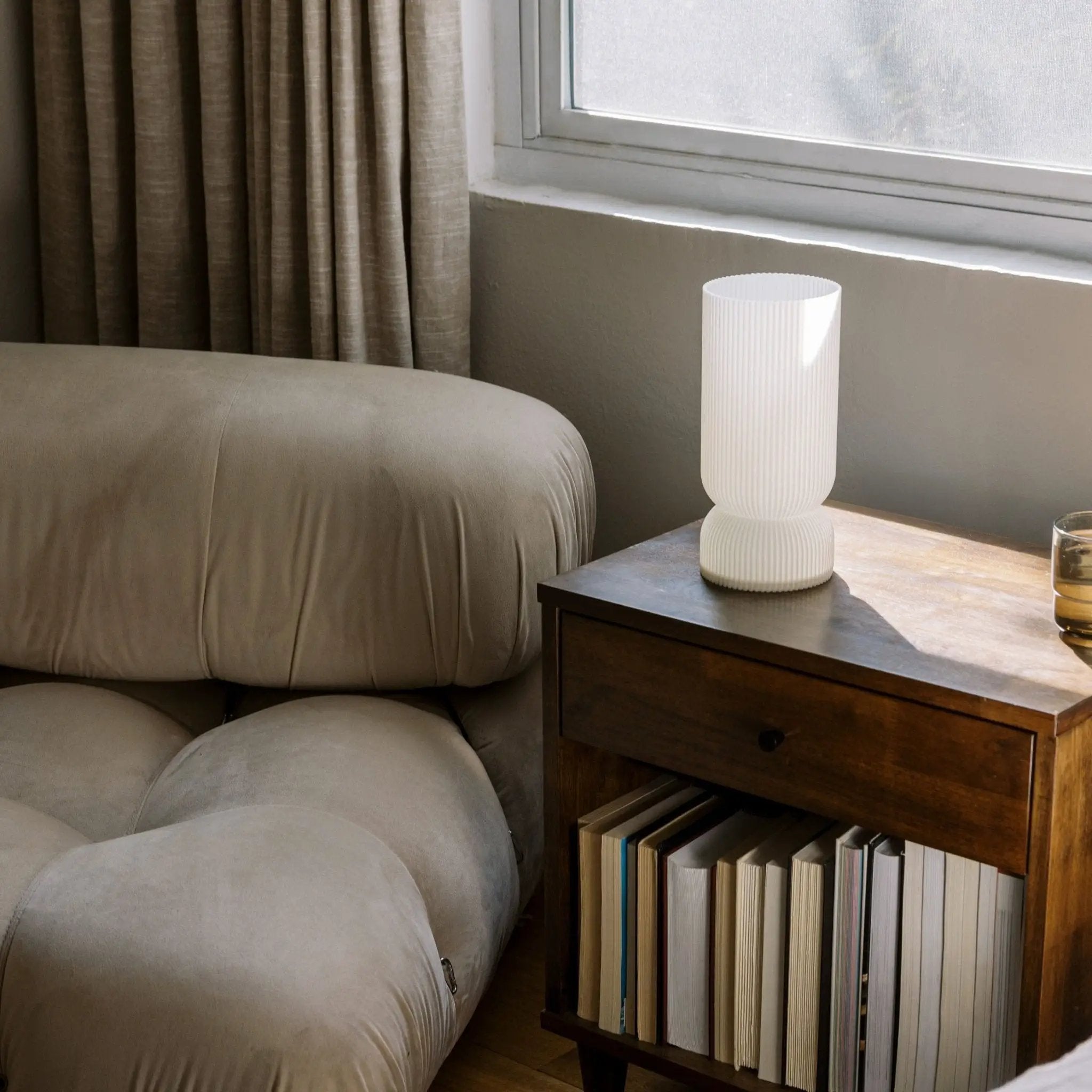 Stance table lamp by Terra Labs; white ribbed ceramic base on dark wood nightstand beside beige sofa.