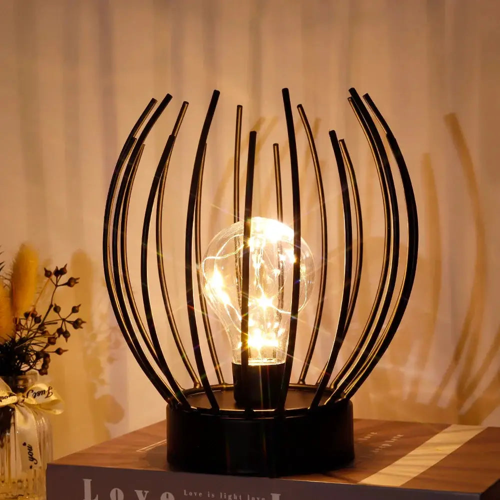 7-inch tall battery-powered table lamp by JHY DESIGN with curved black metal spokes surrounding a clear bulb