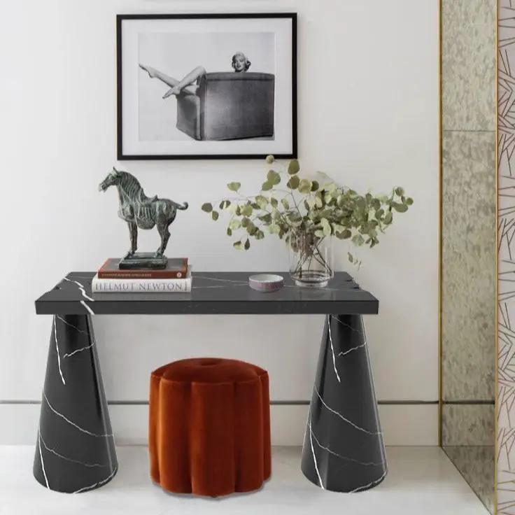 Toros black marble console with cone-shaped legs; decor includes horse statue, books, vase, and orange ottoman.