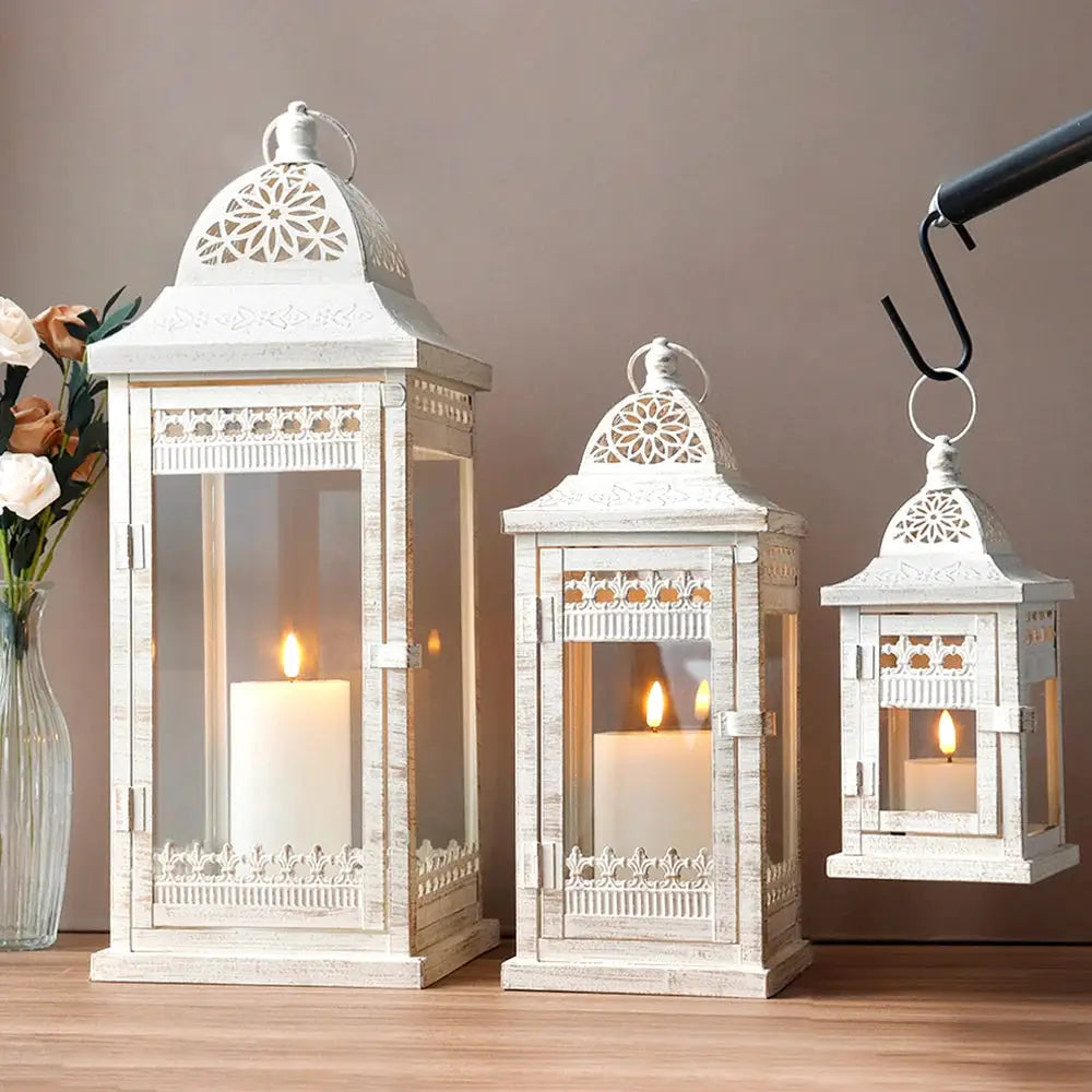 Set of 3 beige distressed metal candle lanterns by JHY DESIGN; 20, 14.5 and 9.5 in tall with lit candles.