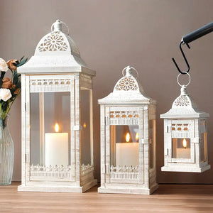 Set of 3 beige distressed metal candle lanterns by JHY DESIGN; 20, 14.5 and 9.5 in tall with lit candles.