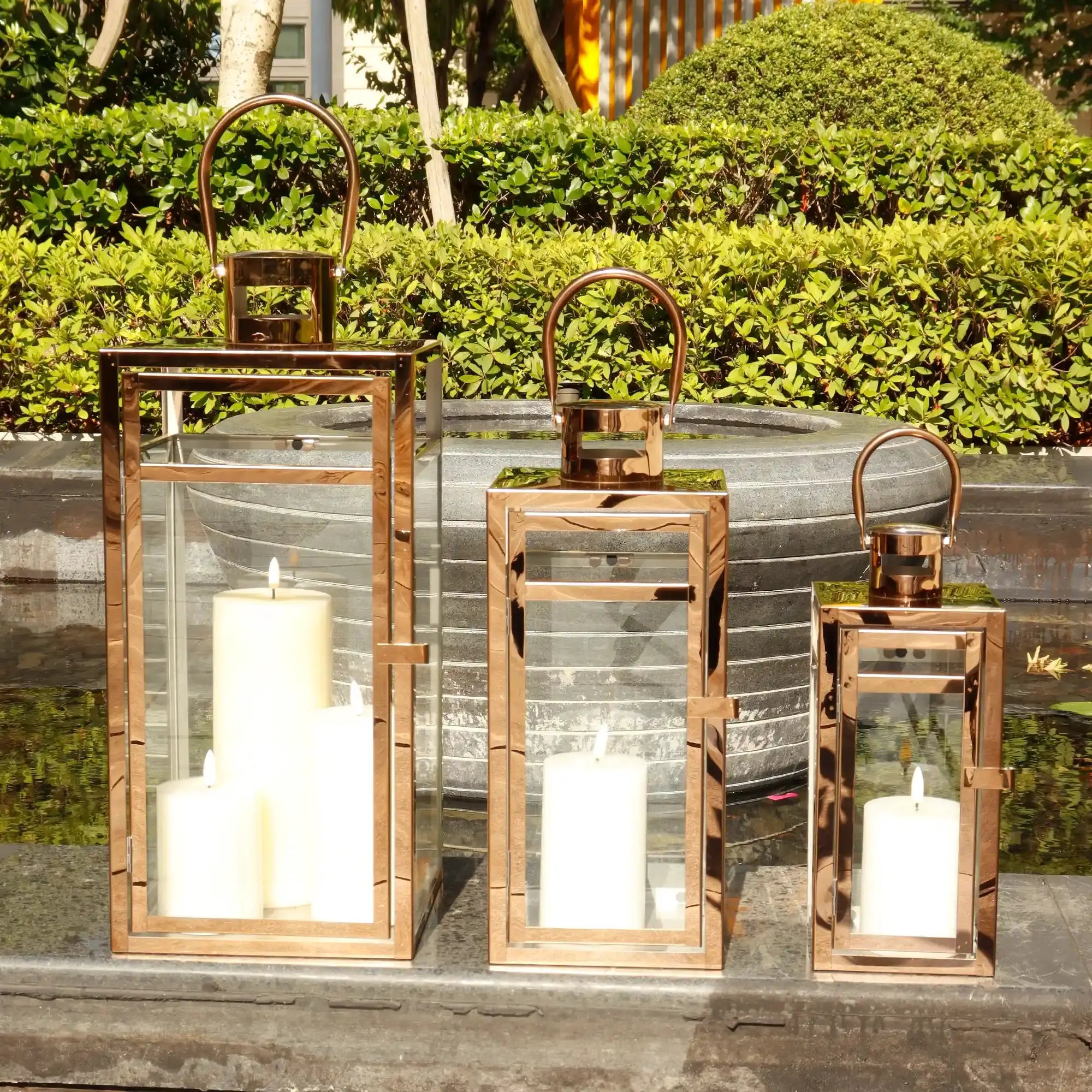 Set of 3 rose-gold stainless steel decorative candle lanterns with glass panels and curved handles