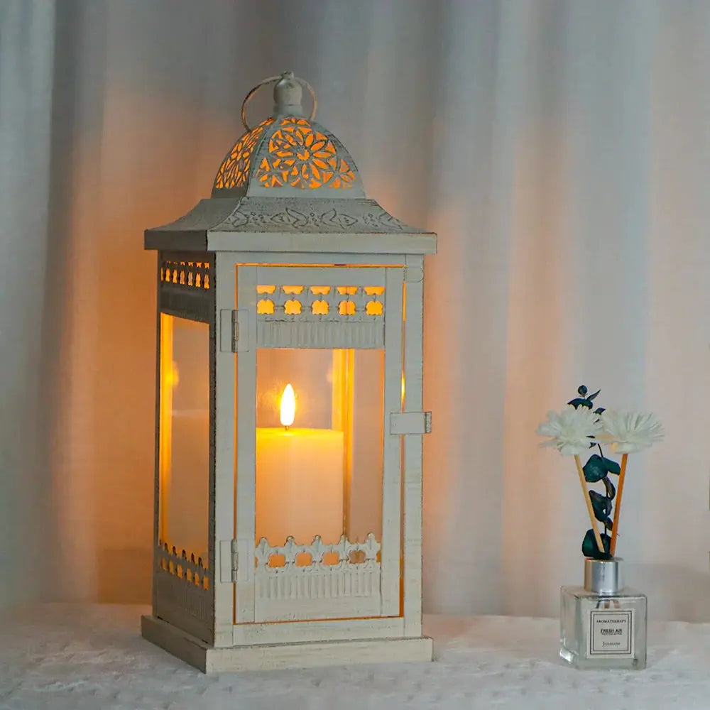 Beige metal decorative candle lantern with gold-brushed accents; 14.5-inch tall, glass panels, lit candle inside