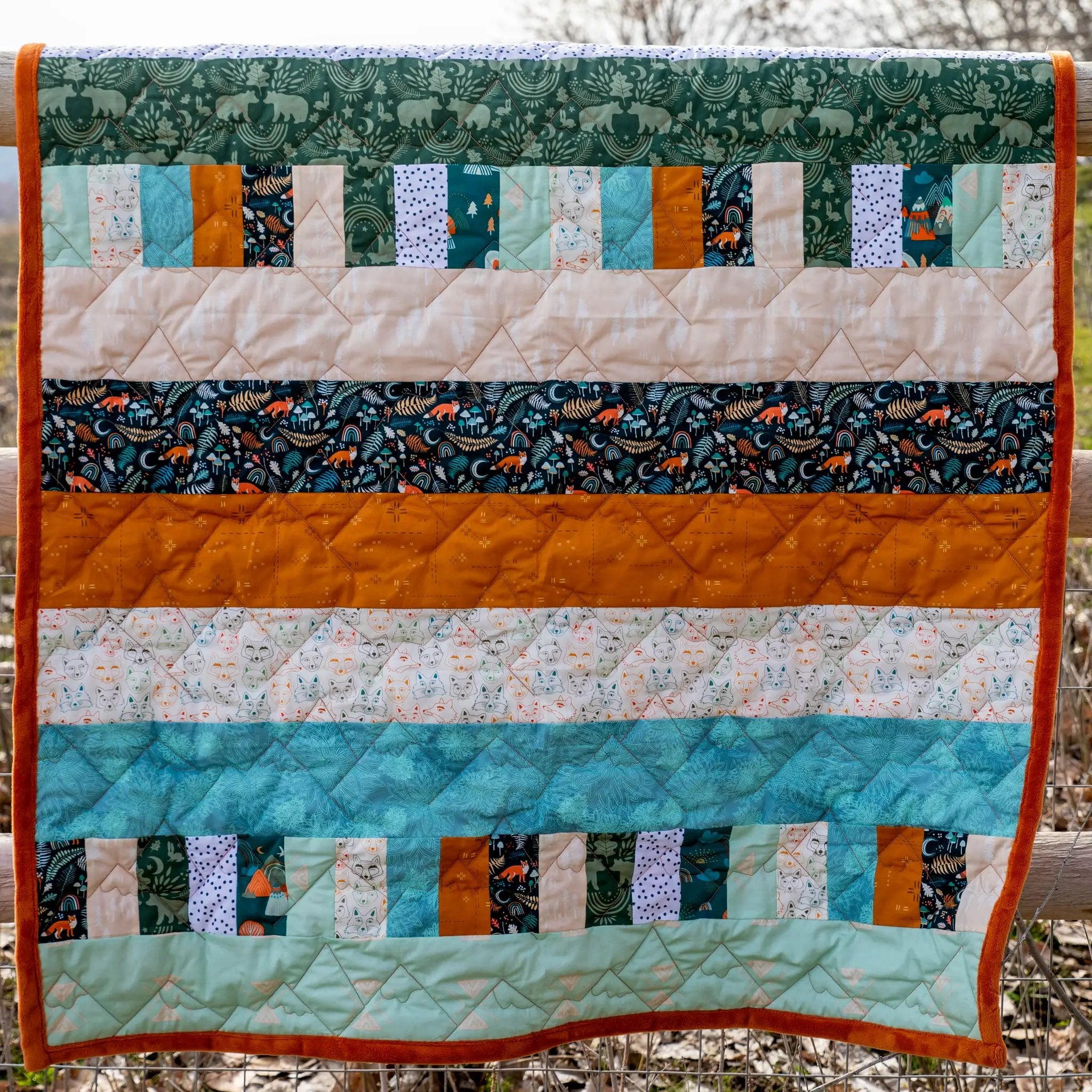 Bricks and Beams Quilt Kit Timberline by Block Party Quilt Co; vibrant patchwork with teal greens and orange binding.