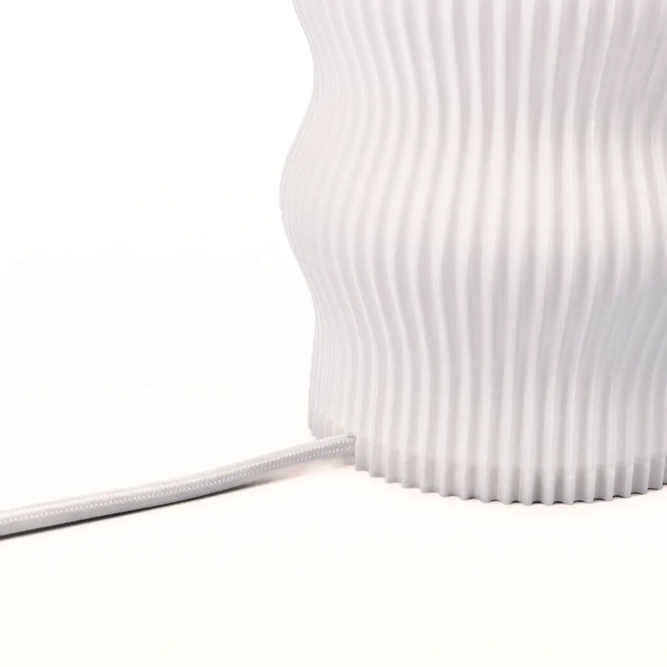Wub Table Lamp by Terra Labs, white ribbed surface with cloudlike waves; power cord visible.