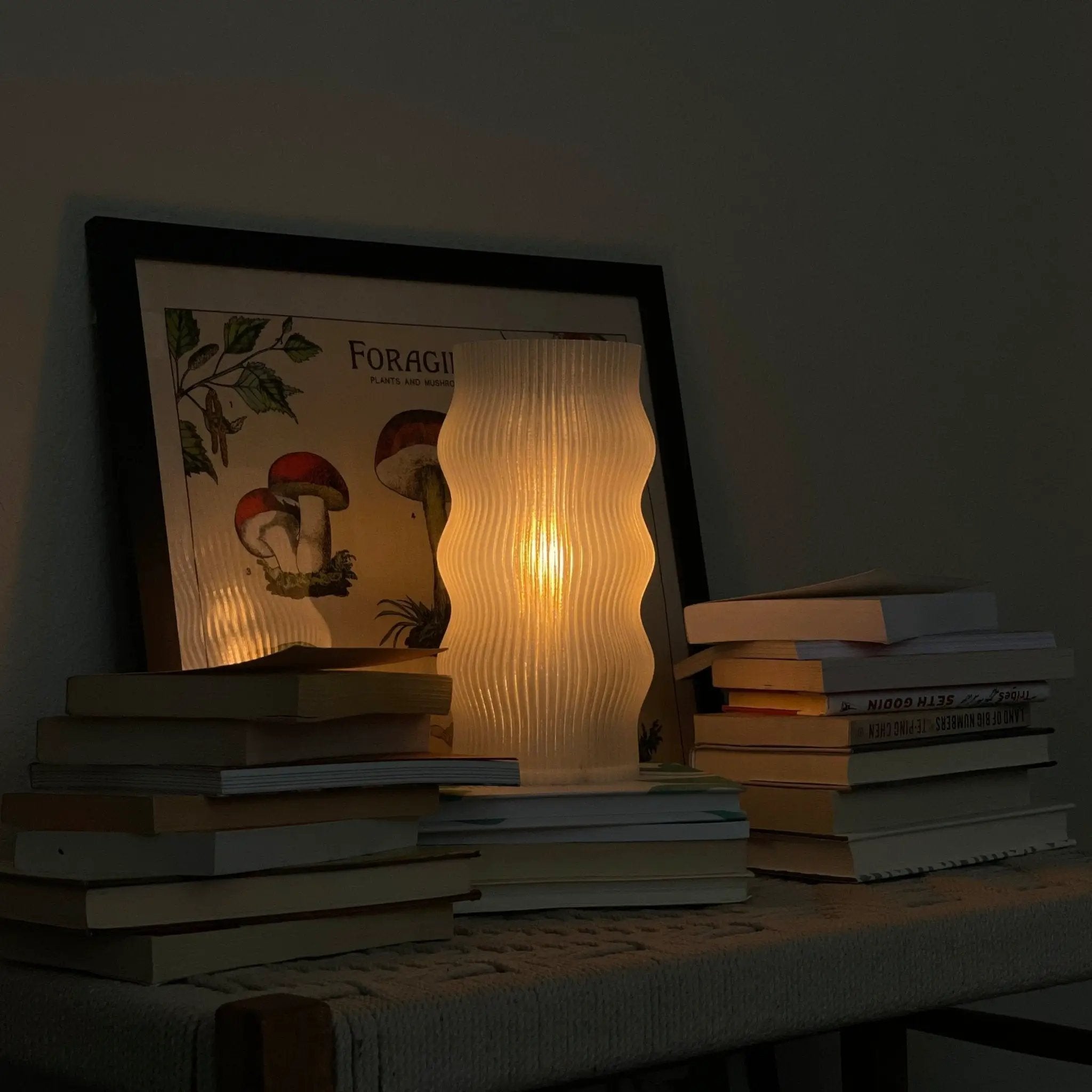 Terra Labs Yuji table lamp with white ribbed glass and warm glow beside a framed botanical print and books.