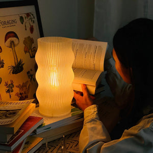 Yuji table lamp by Terra Labs, white ribbed ceramic with warm glow on a shelf.